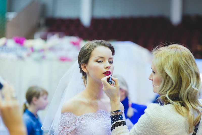 невеста с фотой, которой делают макияж для свадьбы